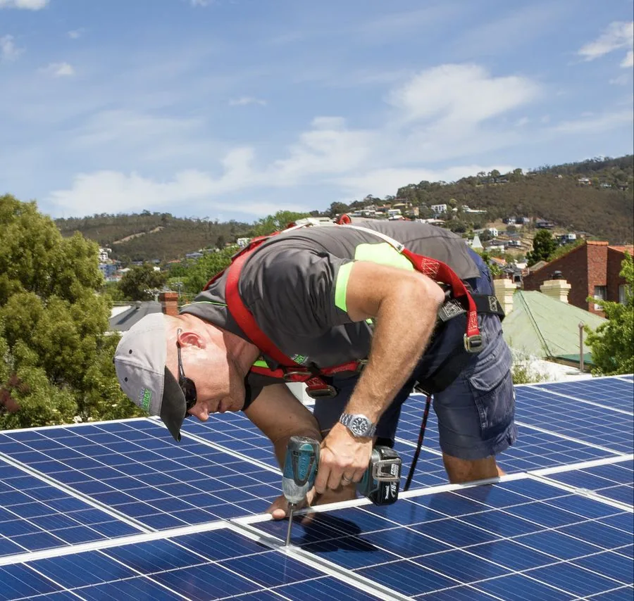 REST Energy installer in a safety harness working on solar panels with Hobart's hills behind